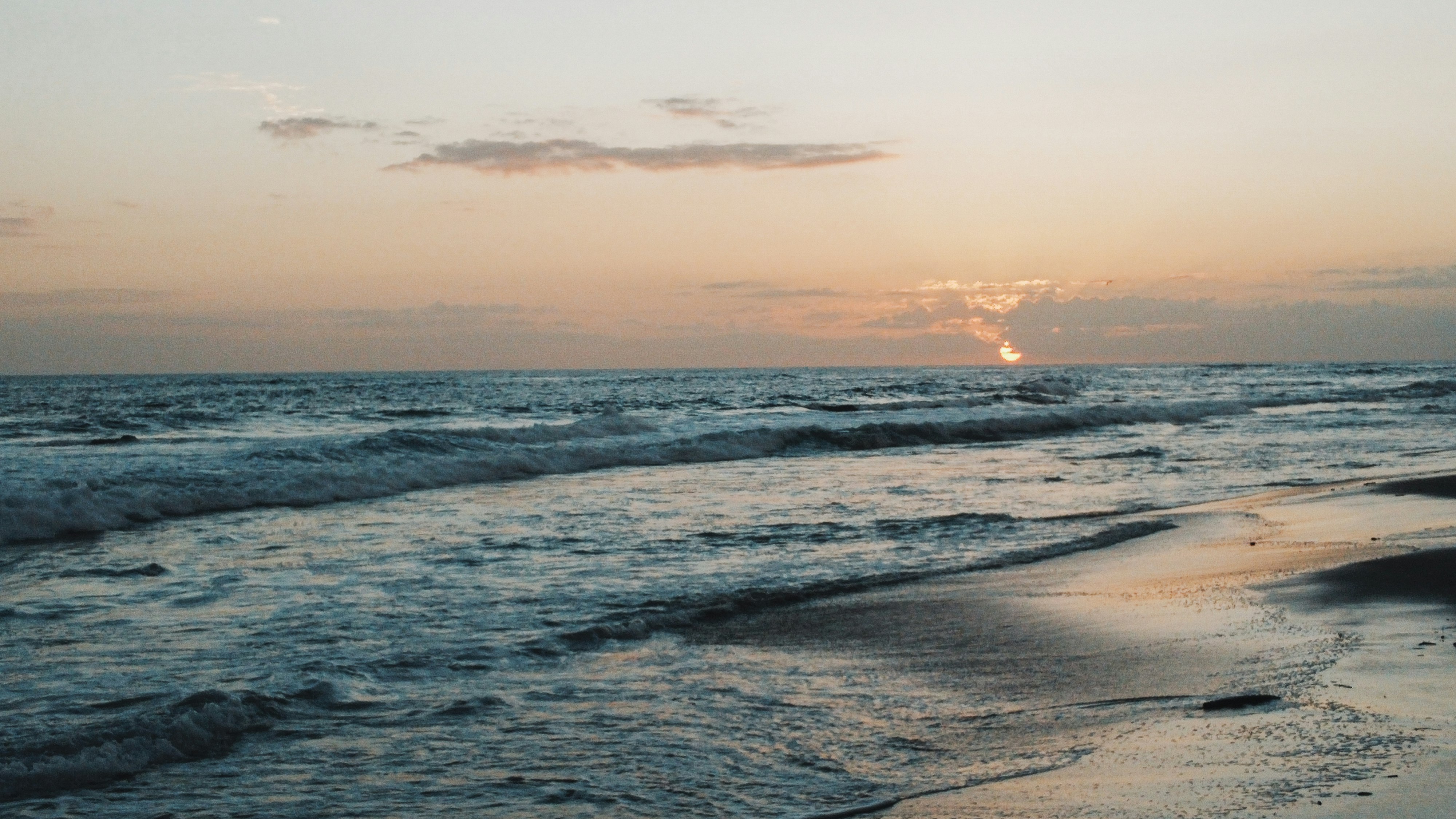 ocean waves crashing on shore during sunset